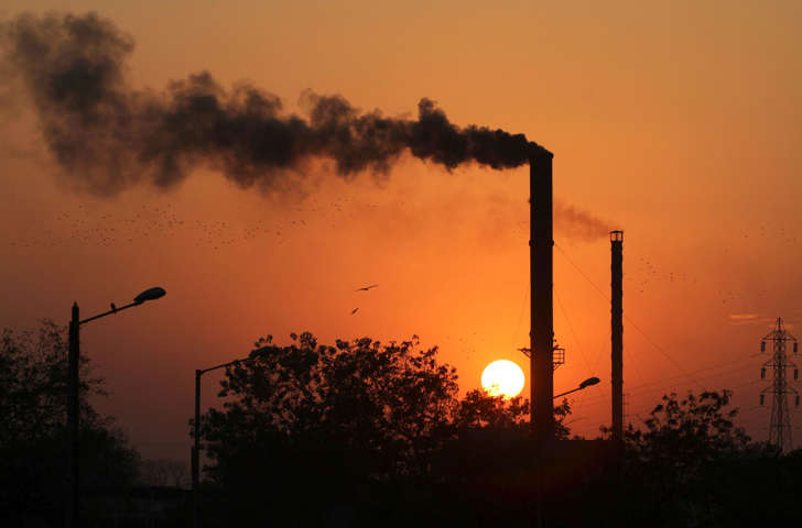 Birds fly past at sunset as smoke leaves a chimney at a factory in Ahmadabad, India, Monday, Dec. 8, 2014.