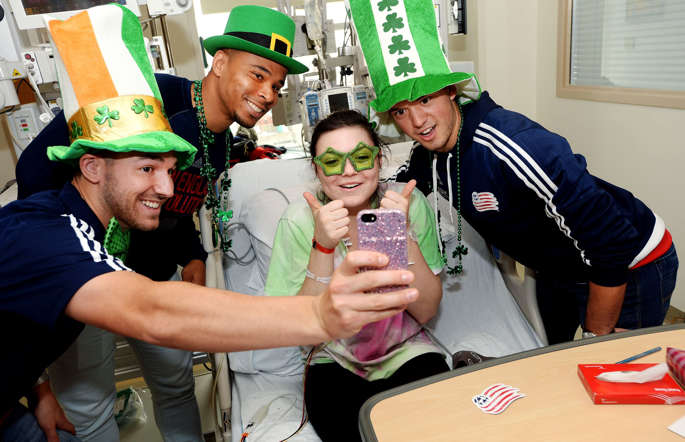 New England Revolution (L to R) Tyler Rudy, Charlie Davies, and Kelyn Rowe take a selfie with Belle at Boston Children's Hospital March 10, 2015 in Boston, Massachusetts.