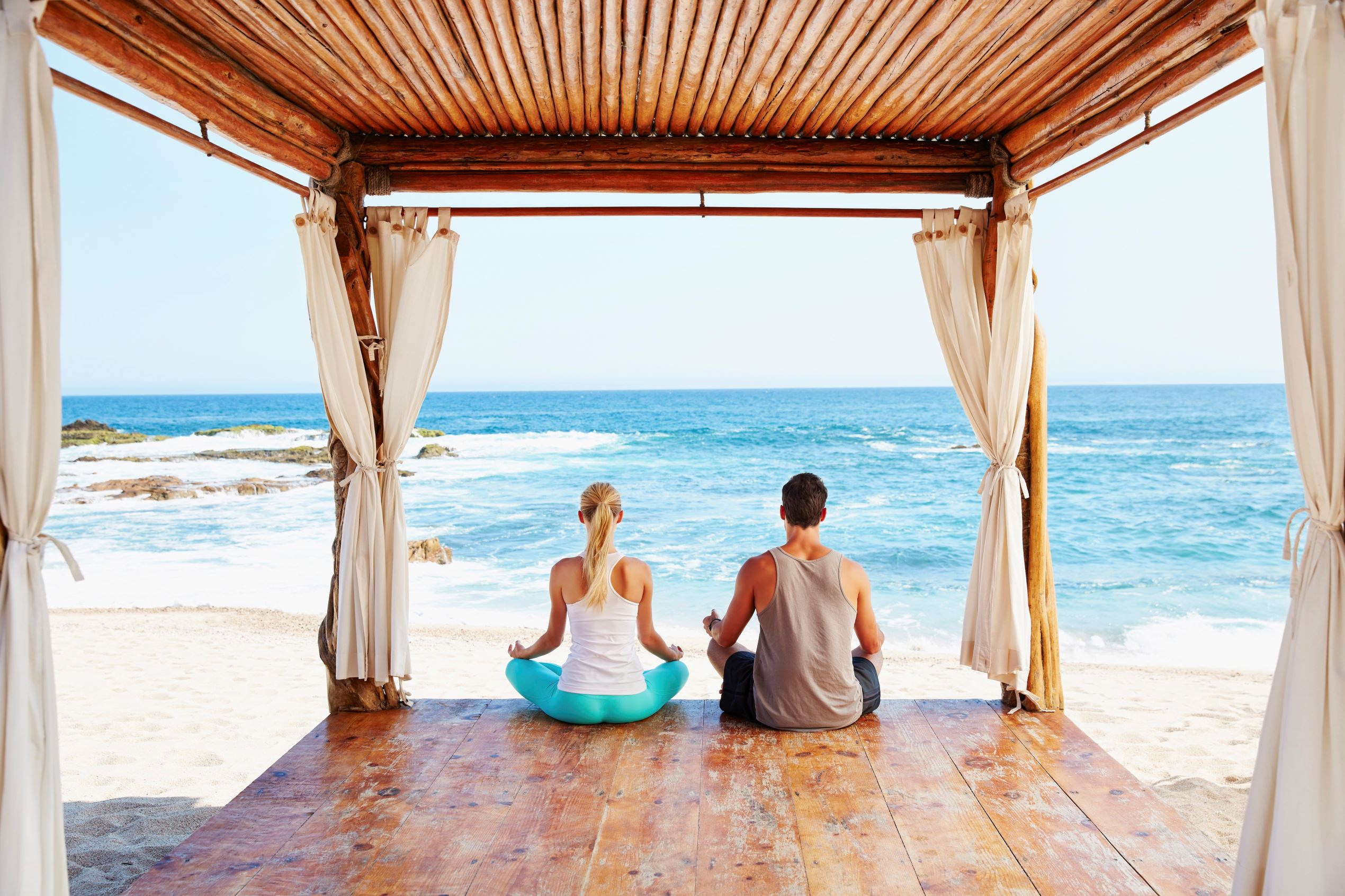 Couple meditating together in cabana overlooking ocean