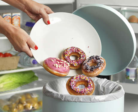 Woman disposing of donuts in trash bin. Peter Dazeley/Getty Images