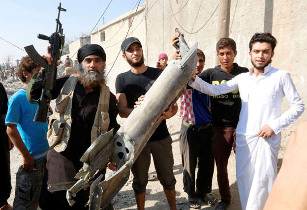 An Islamic State militant (L) stands next to residents as they hold pieces of wreckage from a Syrian war plane after it crashed in Raqqa, in Syria September 16, 2014.