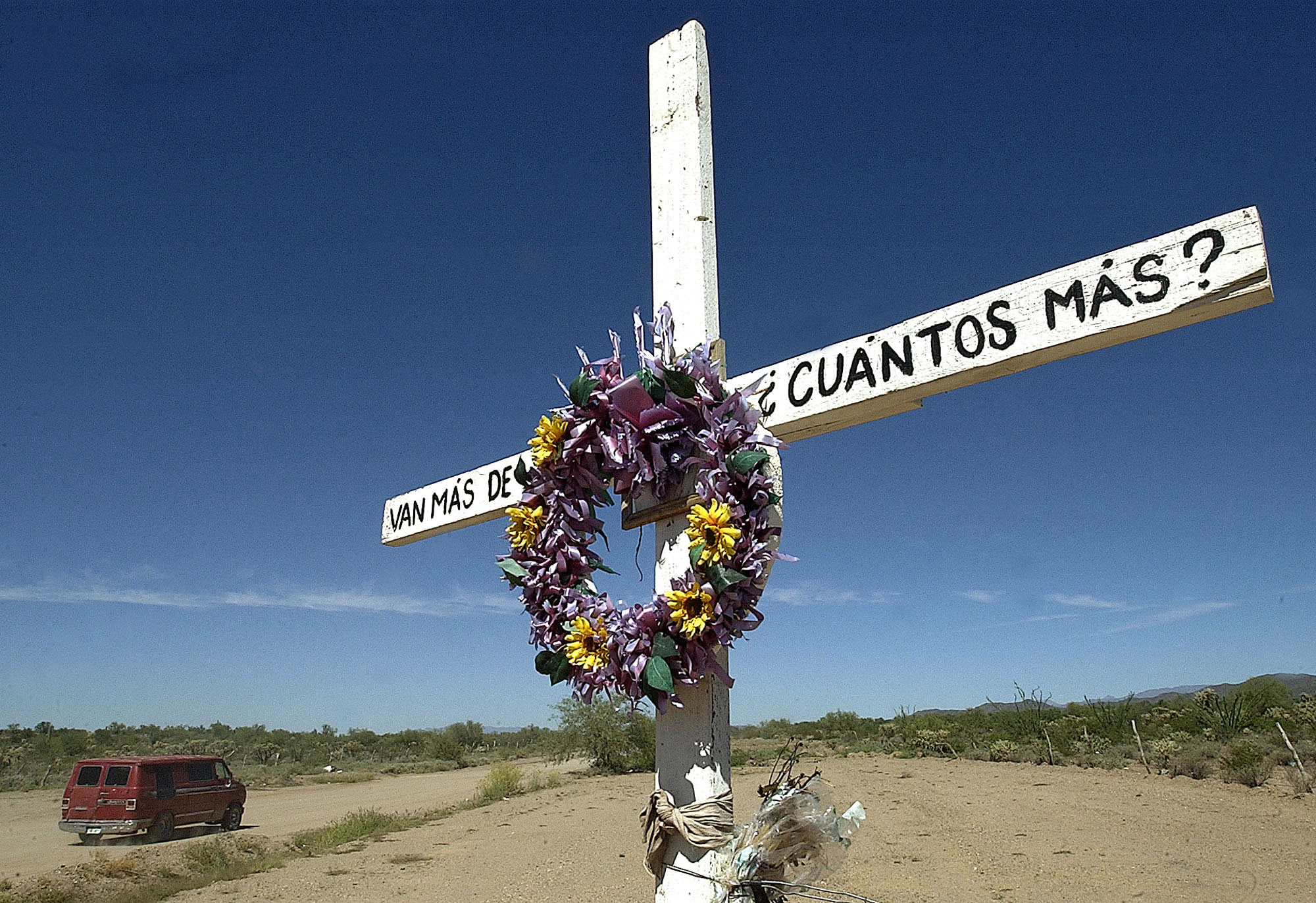 A van load of migrants travel past a memorial asking "How many more have to die?" along the toll road from Altar, Sonora to Sasabe, Sonora, Mexico. The road is mainly used to shuttle migrants by the van load seeking illegal entry into the United States.
