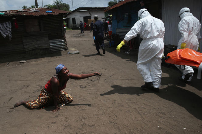 THÁNG MỘT 2014 TRỞ ĐI: BÙNG NỔ DỊCH EBOLA Ở TÂY PHI Khởi phát tại Guinea vào cuối năm 2013, đại dịch Ebola ở Tây Phi lan sang các nước láng giềng Liberia và Sierra Leone. Theo ước tính của Tổ chức Sức khỏe Thế giới, đến trước tháng 11, đại dịch lớn nhất ltorng lịch sử này đã cướp đi 7000 mạng người. Trong ảnh là một phụ nữ ném nắm cát về phía xác của chị gái mình trong lúc một đội chôn cất nạn nhân Ebola khiêng xác đi hỏa thiêu ở  Monrovia, Liberia.