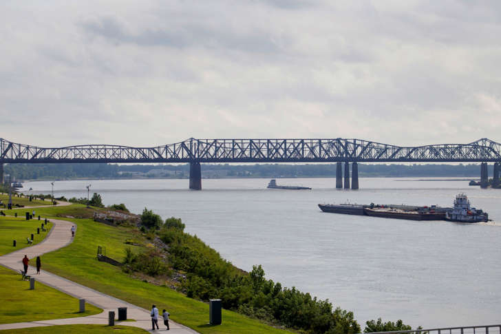 A barge moves along the Mississippi River towards the Memphis-Arkansas bridge.