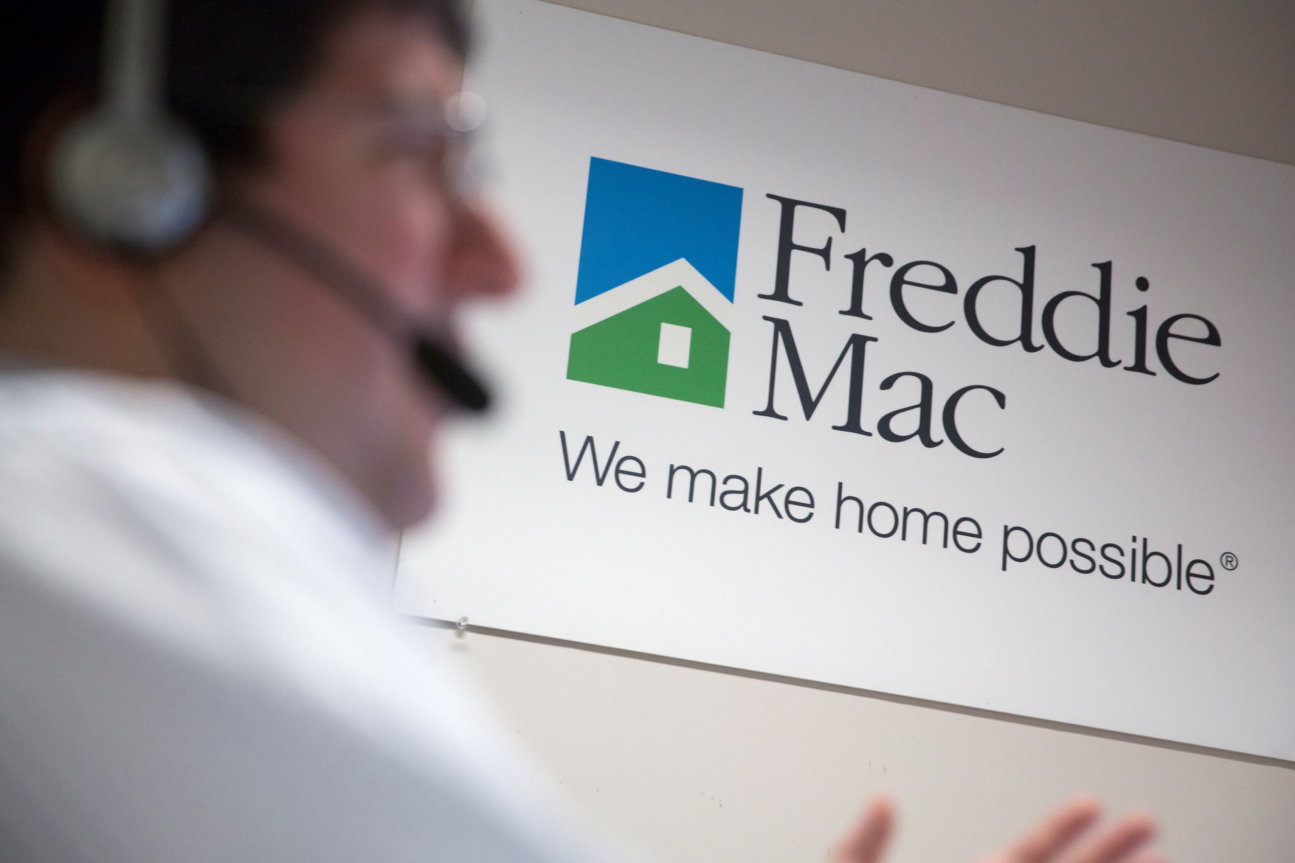A Freddie Mac sign hangs behind employee John Estrada as he works in the borrower contact unit area at Freddie headquarters in McLean, Virginia, U.S., on Tuesday, April 8, 2014.
