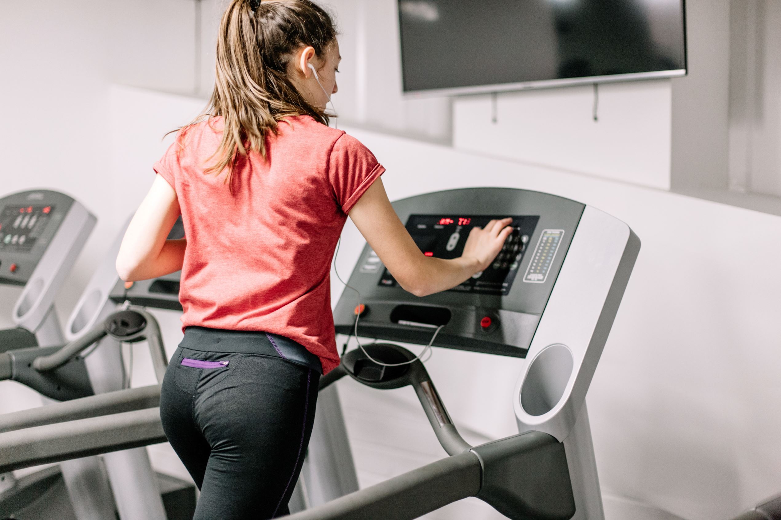Young female operating a treadmill, wearing earphones