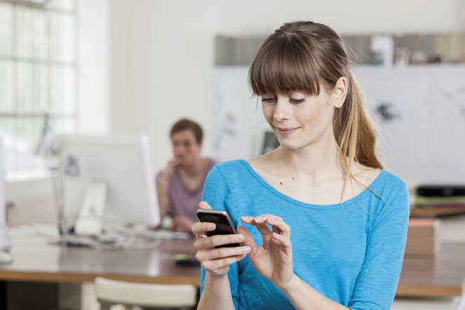 Portrait of young woman in an creative office using her smartphone