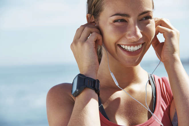 A cheerful young woman putting her earphones in before a running session