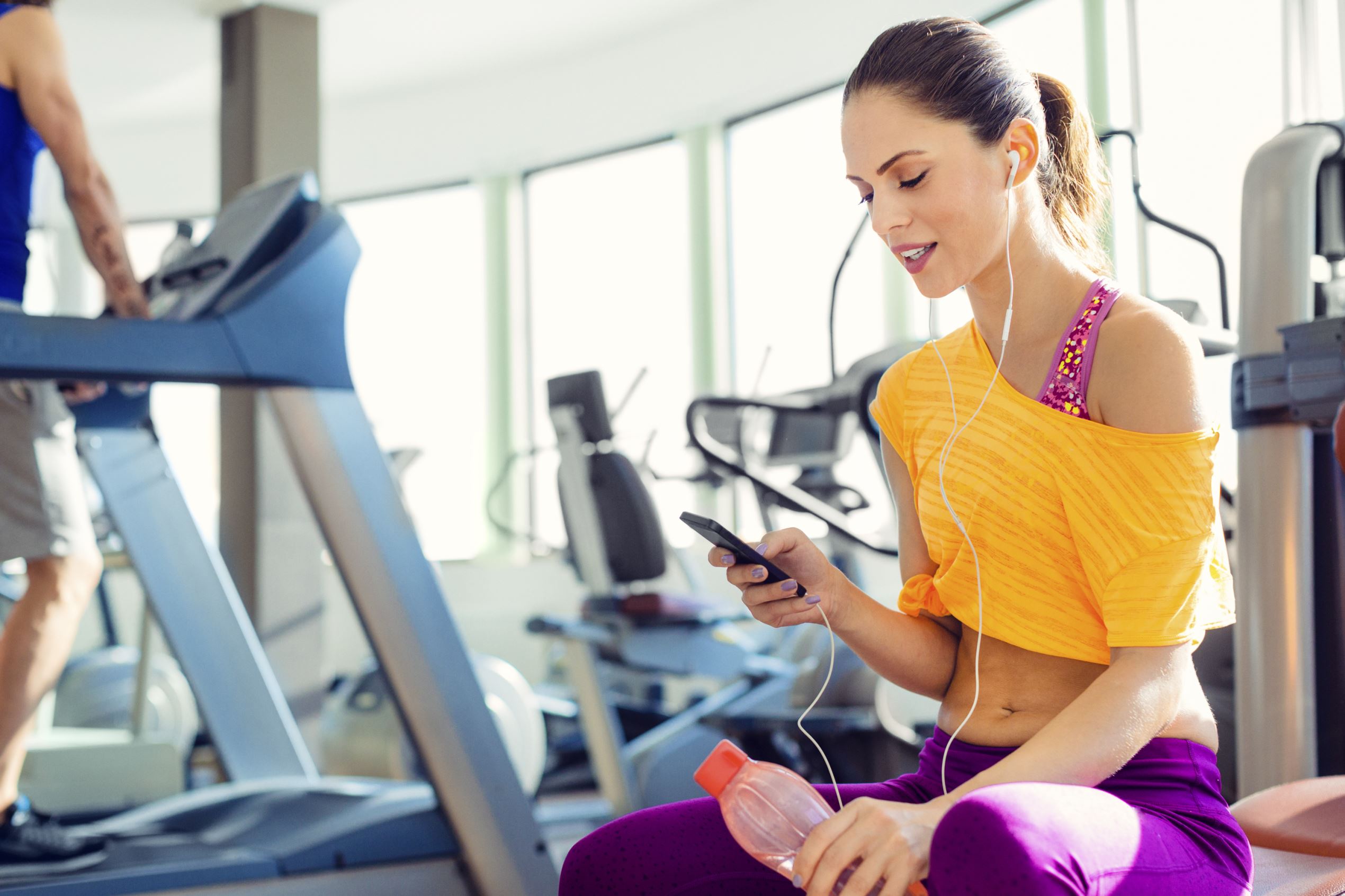 Young female holding smart phone and listening music in the gym.