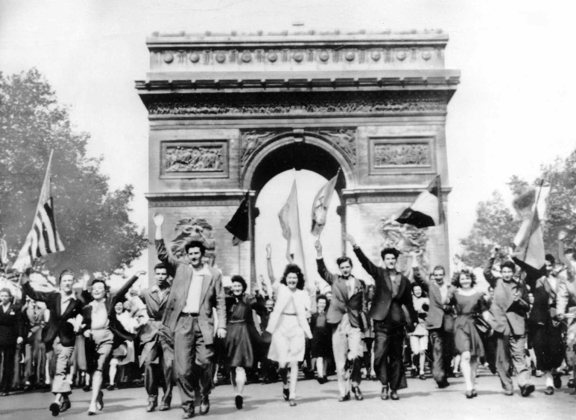 Parisians march through the Arc de Triomphe jubilantly waving flags of the Allied Nations as they celebrate the end of World War II on May 8, 1945.  German military leaders signed an unconditional surrender in Reims, France, on May 7.