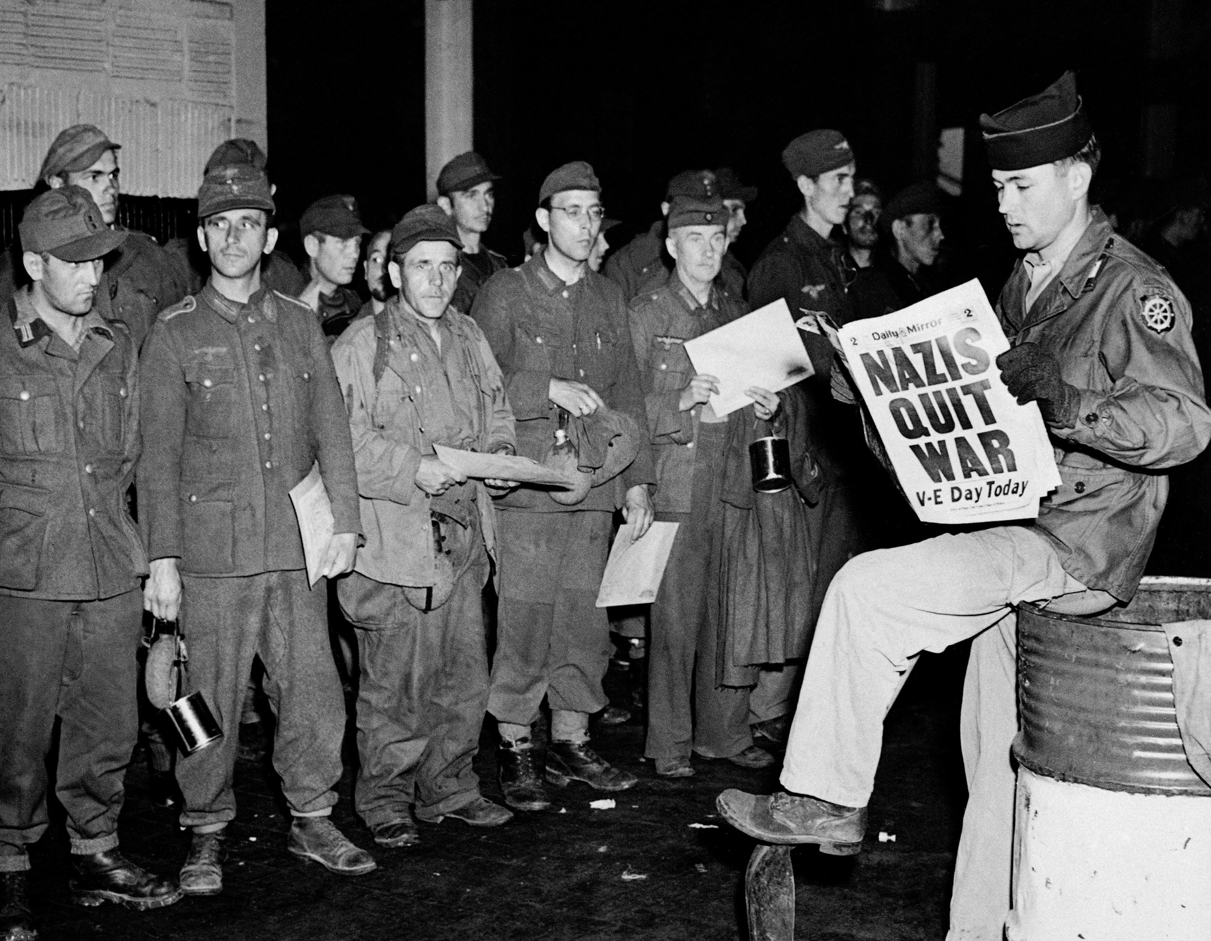 Pfc. Clarence K. Ayers of Evansville, Ind., reads the news of V-E Day as newly arrived German prisoners stand on a New York City pier, May 8, 1945.