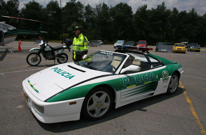 A national police officer sits in a Ferrari painted with the logo of the national police as it is displayed at a commercial center in Bogota, Colombia, Saturday Feb. 18, 2012.  The car was converted into an exhibition police car after it was seized from drug trafficker Hernando Gomez, alias "Rasguño," or "Scratch," who was extradited to the U.S. where he is currently serving time. (AP Photo/William Fernando Martinez)